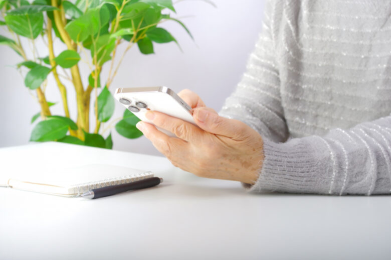 グレーのニットを着た高齢の女性が、スマートフォンで検索をしている様子